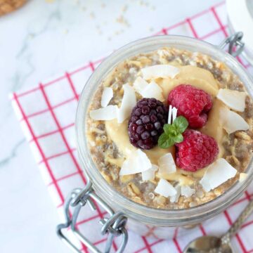 Overnight quinoa oats in jar with peanut butter, frozen fruit, and coconut flakes.