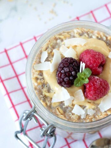 Overnight quinoa oats in jar with peanut butter, frozen fruit, and coconut flakes.