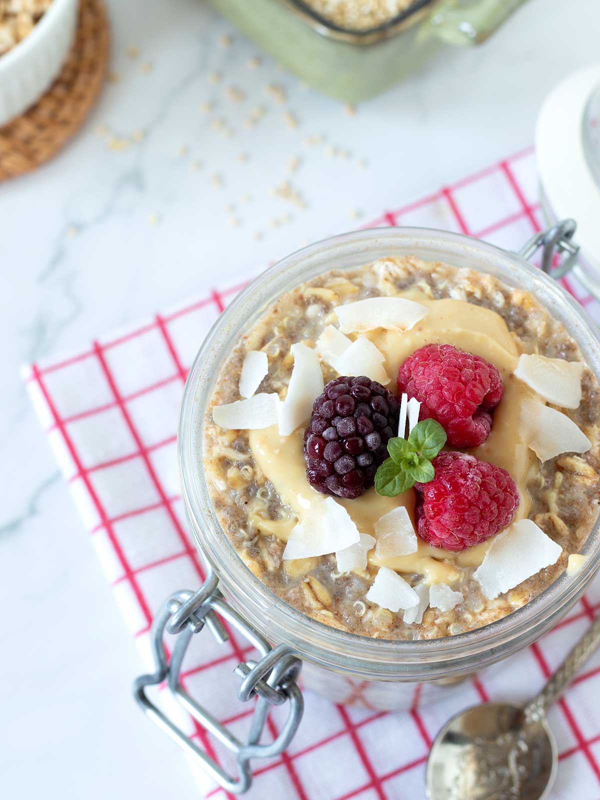 Overnight quinoa oats in jar with peanut butter, frozen fruit, and coconut flakes.