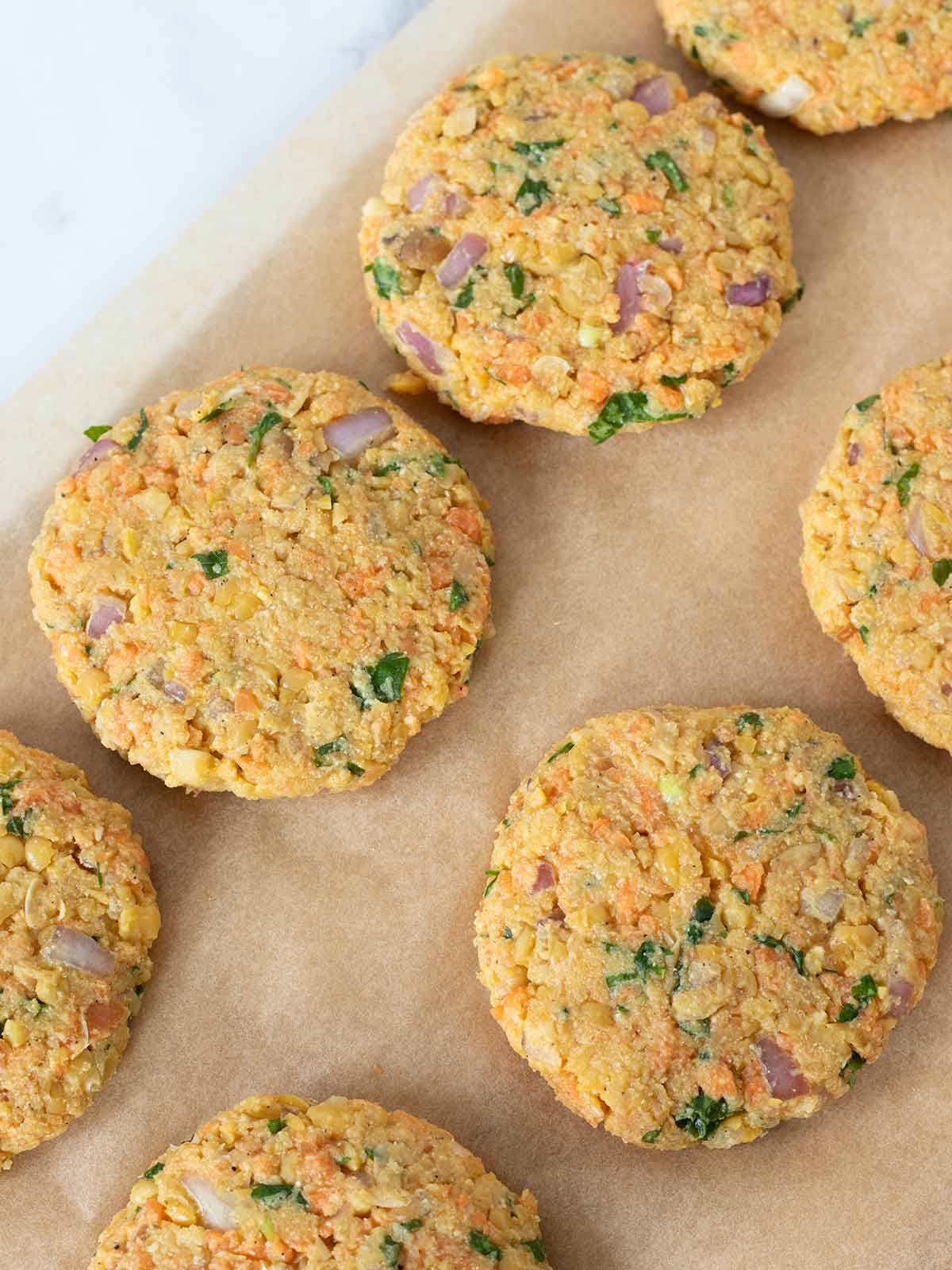 Uncooked chickpea fritters with vegetables on parchment paper.
