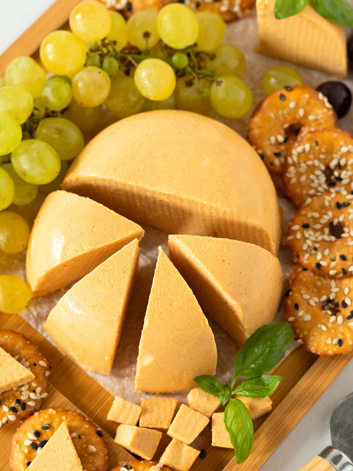 Vegan cheddar cheese slices on snack board with crackers and grapes.