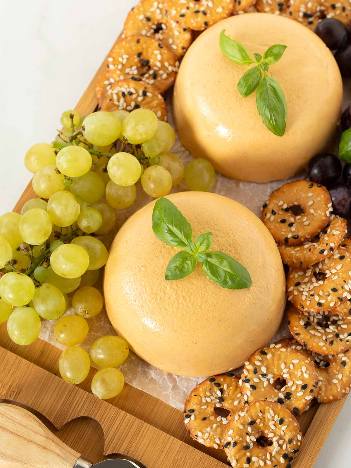 Homemade cashew cheddar cheese on a snack board with crackers and grapes.