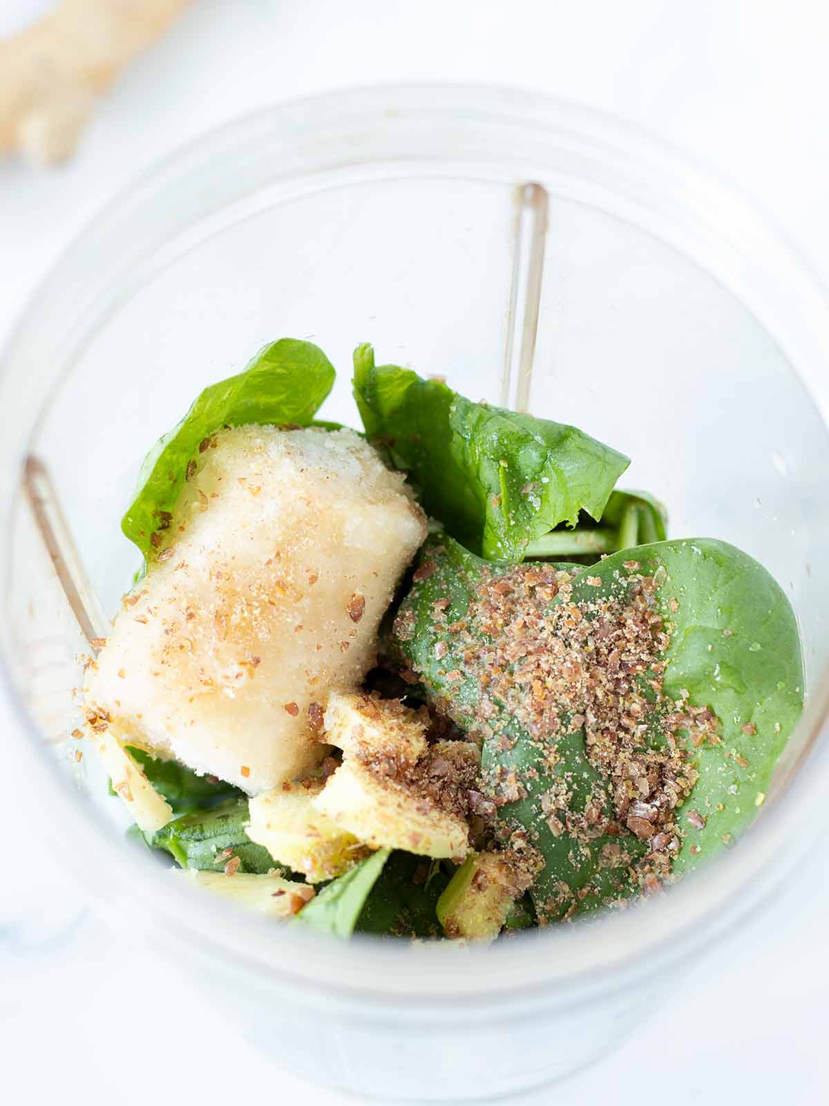 Lemon ginger spinach banana smoothie ingredients in blender cup.