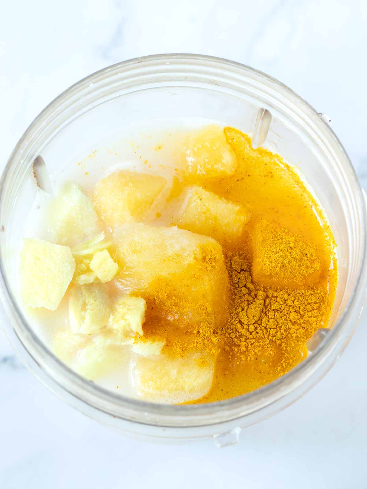 Pineapple ginger turmeric smoothie ingredients in blender cup.