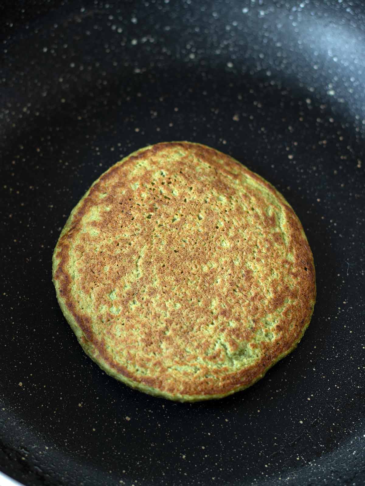 Cooking green banana spinach pancake in non stick pan.