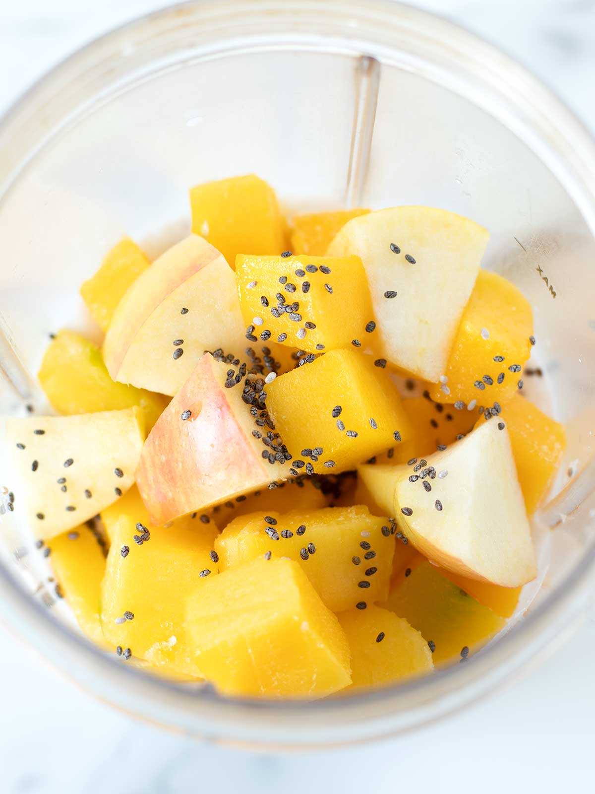 Mango and apple smoothie ingredients in blender cup.