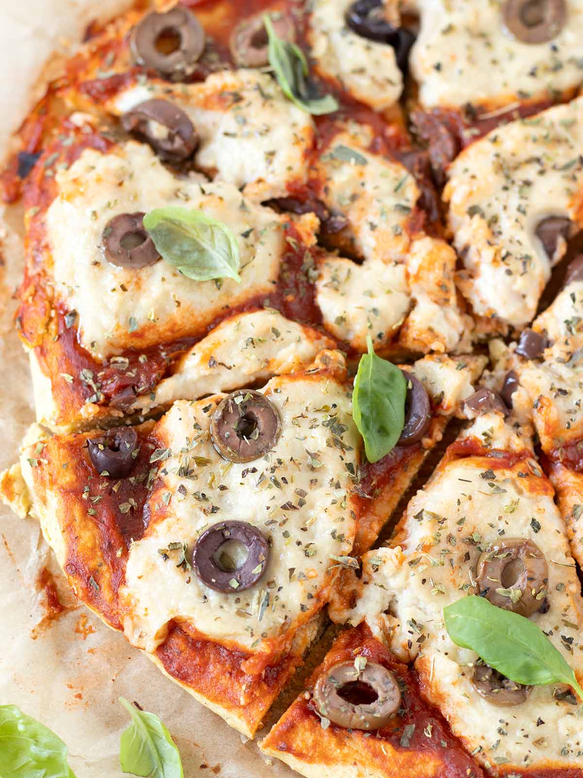 Gluten-free chickpea flour pizza crust topped with vegan mozzarella, tomato sauce, olives, and basil leaves.