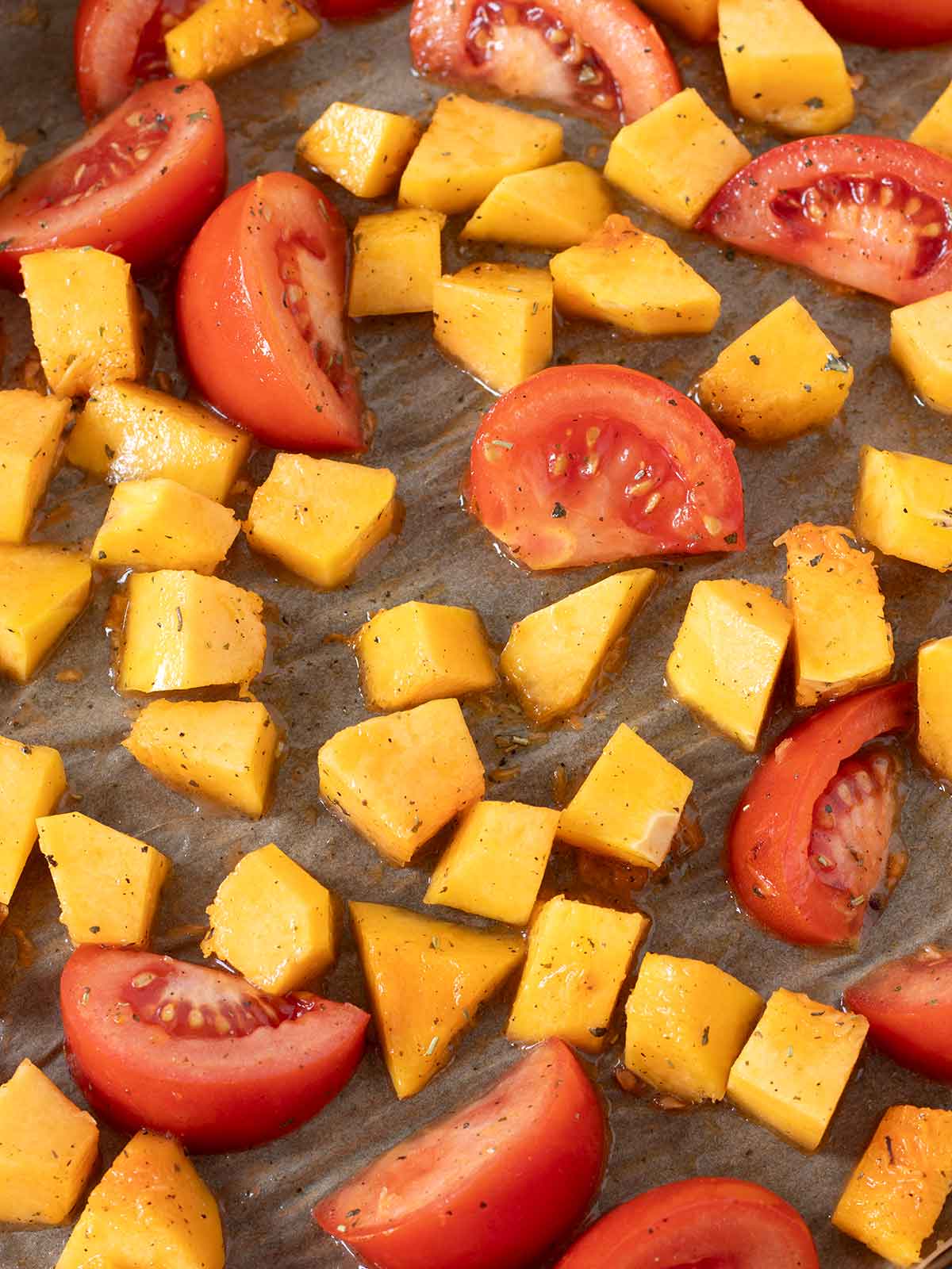 Fresh chopped tomatoes and butternut squash on baking sheet prepared for roasting.