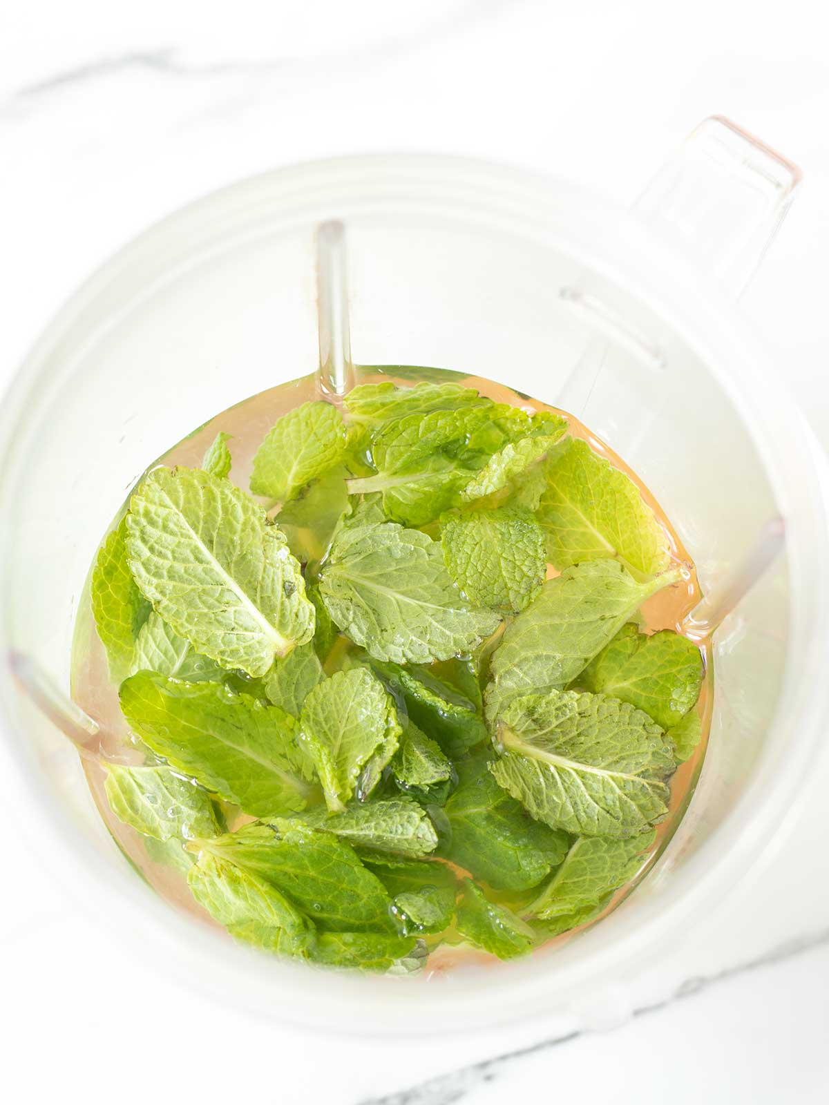 Fresh mint, lemon juice, maple syrup and water in a blender for homemade lemonade drink recipe.