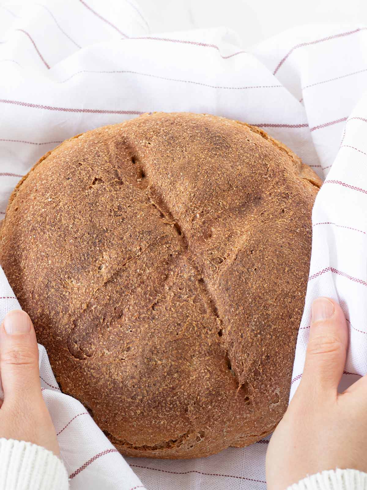 Rustic whole wheat bread wrapped in kitchen towel.