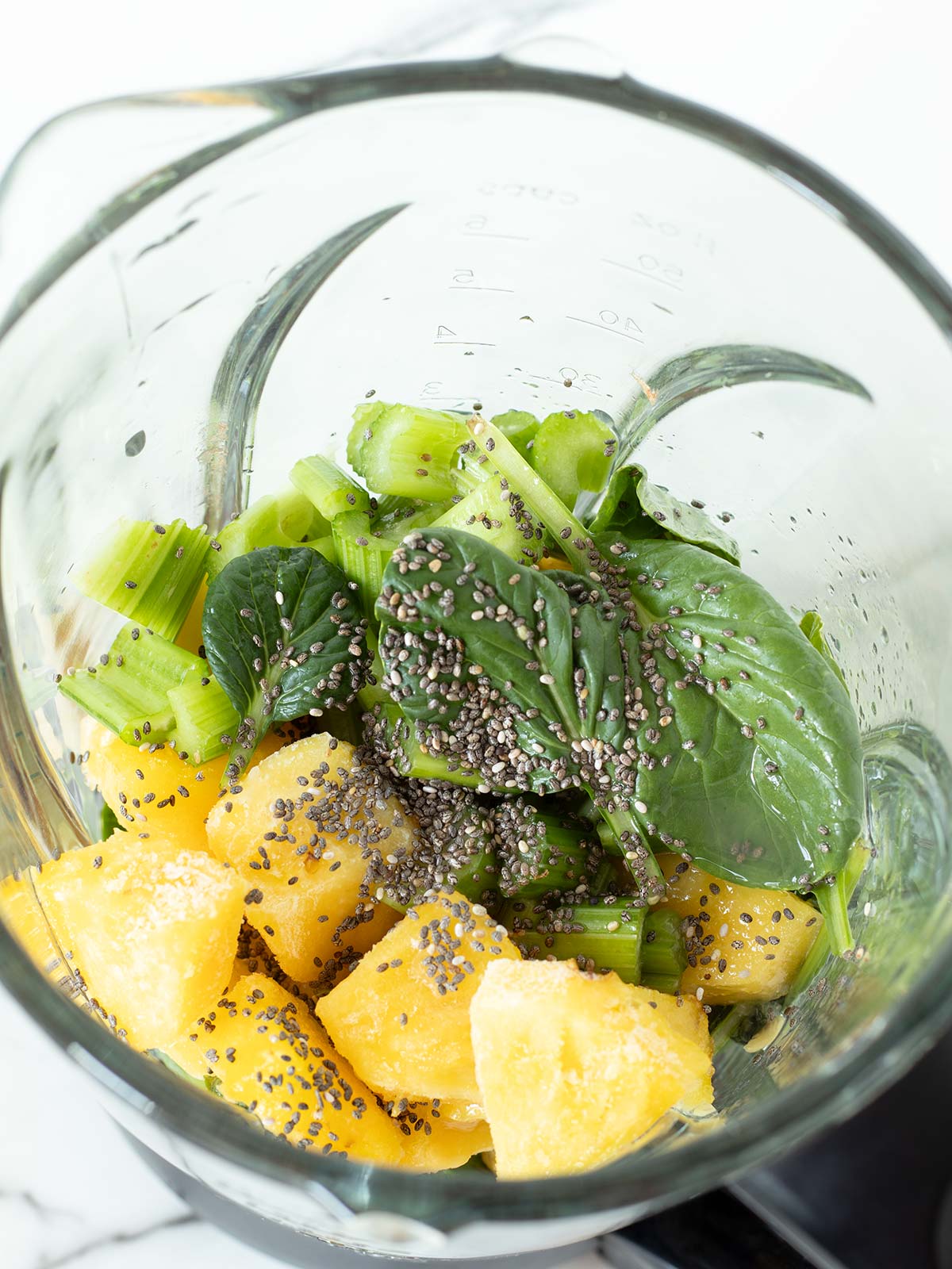 Spinach celery pineapple smoothie ingredients in a blender.