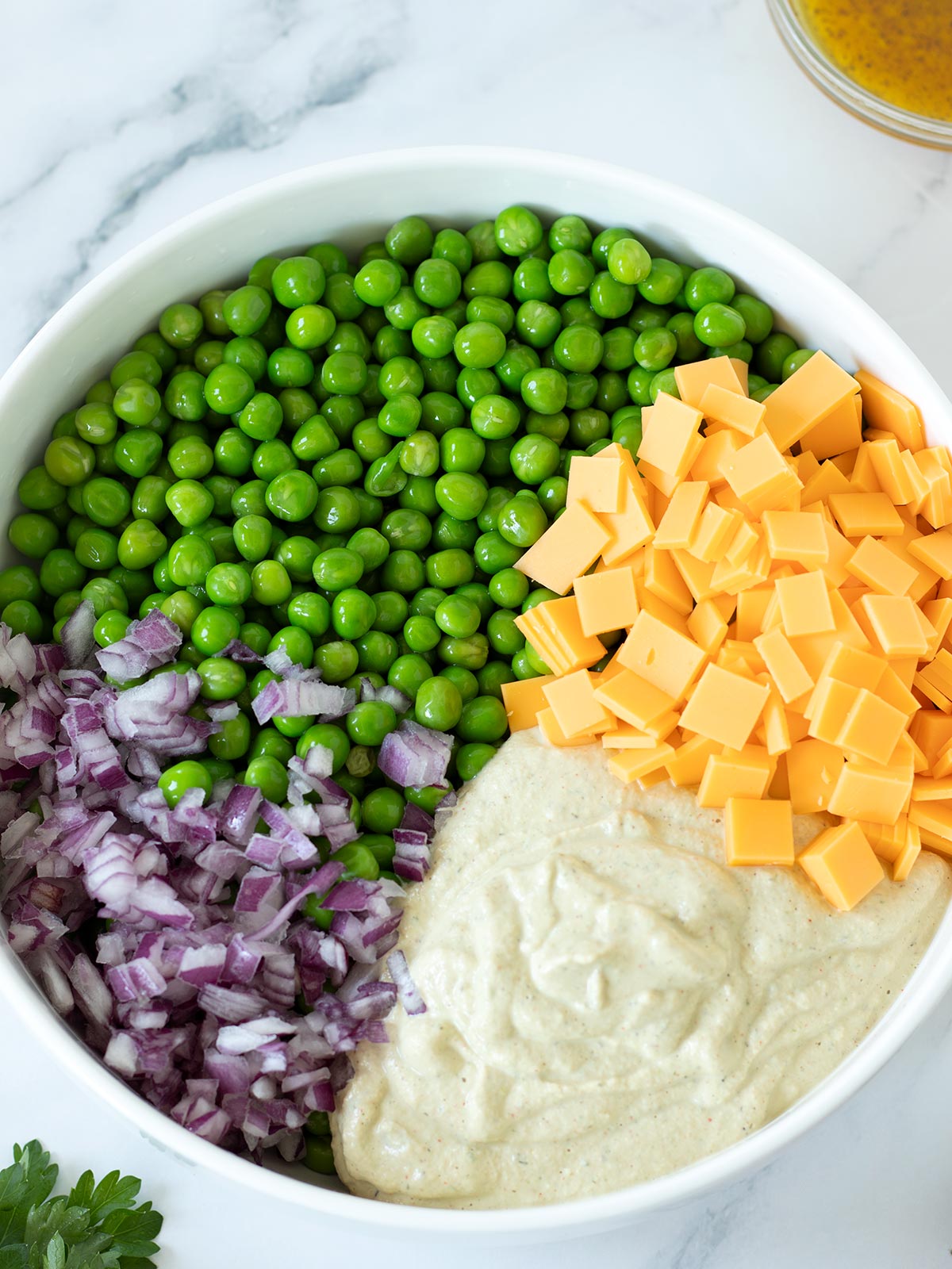 Ingredients for vegan green pea salad with cheddar cheese in a bowl.