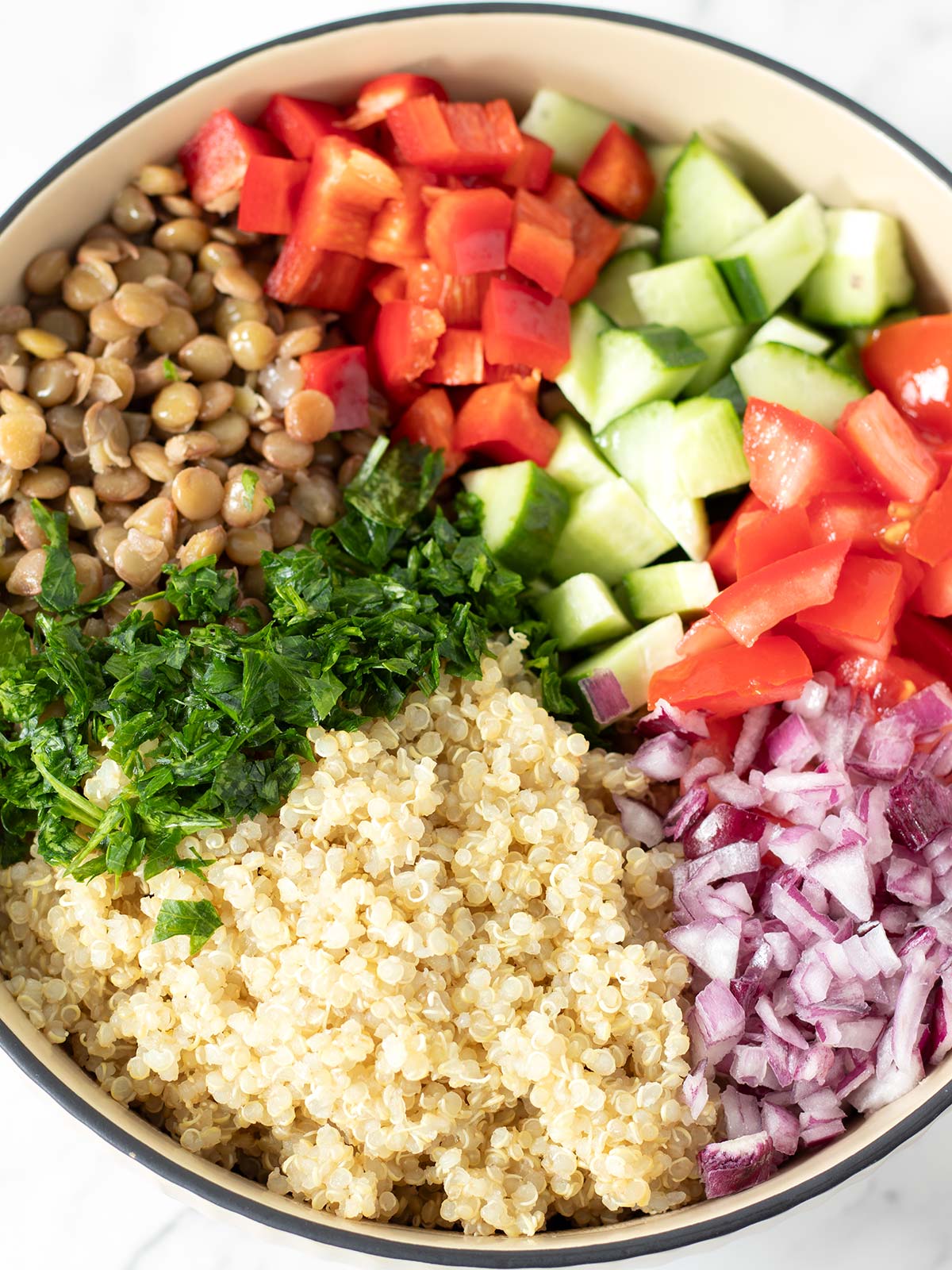 Chopped vegetables, quinoa, and lentils in a salad bowl.