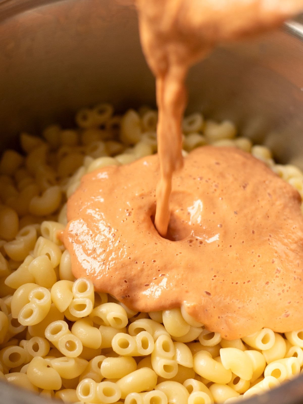 Pouring creamy silken tofu tomato sauce on top of pasta.